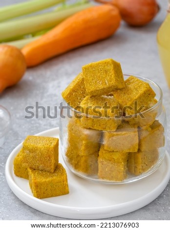 Homemade vegetable bouillon cubes made of braised onion, carrot, celery sticks and salt served in glass jar with ingredients on background. Vertical, selective focus.