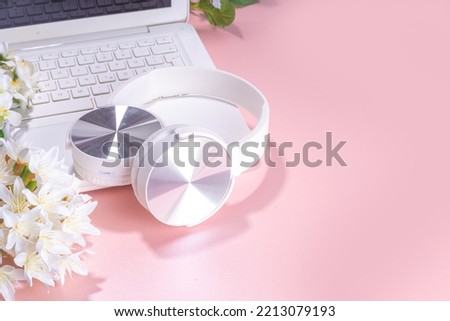 Spring office workplace, blogging flat lay background. White laptop, with headphones, tablet, spring flowers bouquet on pink pearl background, girl's hands typing on a laptop.