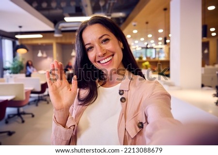 POV Selfie Portrait Of Waving Businesswoman Standing In Modern Open Plan Office Royalty-Free Stock Photo #2213088679