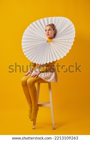 Young indifferent girl in giant jabot collar or neckwear and yellow tights isolated over yellow background. Contemporary art, weird beauty, avant-garde fashion. Royalty-Free Stock Photo #2213109263