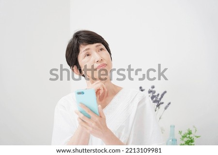 Asian middle aged woman using the smartphone at home Royalty-Free Stock Photo #2213109981
