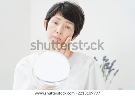 Asian middle aged woman looking in the mirror at home Royalty-Free Stock Photo #2213109997