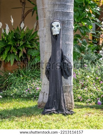 Spooky Halloween decoration of Death leaning against a tree in Los Angeles, CA.