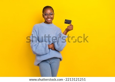Photo of impressed young lady wear blue sweater holding bank card going buy new handbag isolated on yellow color background