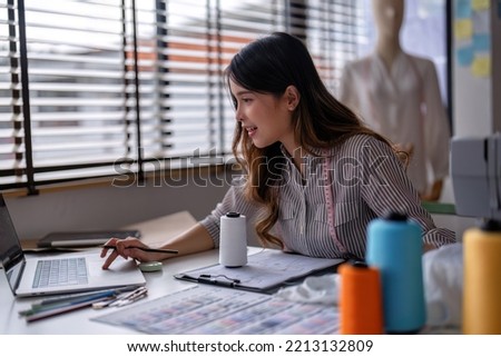 Young professional clothes fashion textile creative thinking designer working on laptop and tablet pc near sewing machine in studio office room