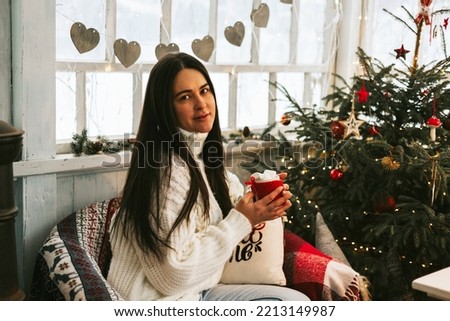 young beautiful brunette woman sit with cup of tea in rustic country house in winter, suburban area with stylish decor, atmosphere of Christmas and New year celebration background, veranda decoration