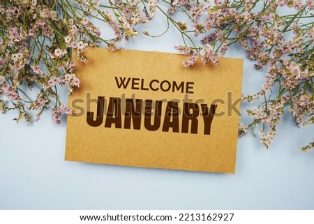 Welcome January written on paper card with flower frame decoraton on pink background