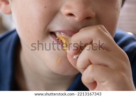 Seven years old boy close up, mouth, nose, and hand, eating bread and enjoying it so much