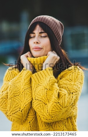 Beautiful European brunette dressed in a yellow woolen sweater and hat outside. The beautiful girl who wears thick stylish autumn clothes in cool weather. Royalty-Free Stock Photo #2213173465