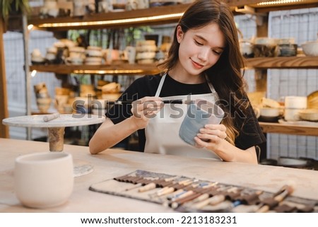 Beautiful young woman holding pottery instrument for scraping, smoothing, shaping and sculpting. Lady siting on bench with pottery wheel and making clay pot