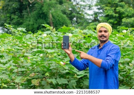 Indian farmer showing smartphone screen at green agriculture field