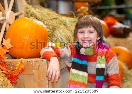 happy boy sits on the hay and hugs the pumpkin at the farm. joyful child celebrates thanksgiving day.