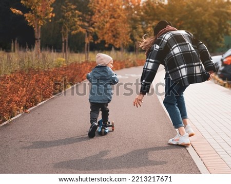 Mother help her son ride with kick scooter. Happy family mother teaches child son to ride a scooter in the Park. Support childhood parenthood idea. happy family concept.