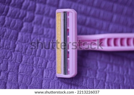 one old plastic pink razor lies on a purple table
