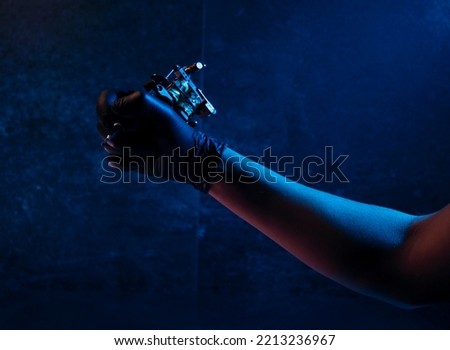 an arm holding a tattoo machine on blue grunge wall