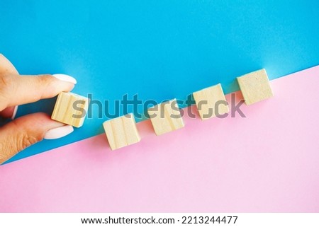 Woman hand arranging empty wood block and copy space on blue and pink background
