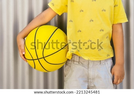 kid dressed in yellow holding on a yellow basket ball