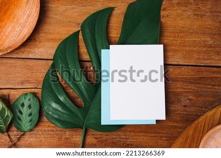business, finance and wedding card concept. Blank white paper with dark wooden table background and leaves. top view, mockup.
