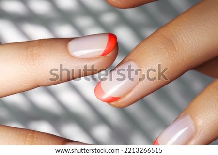 Hands with bright Red French Manicure on Geometric Background. Nails Art Design. Close-up of Female Hands with Trendy Neon Nails on Silver Striped Print Background Royalty-Free Stock Photo #2213266515