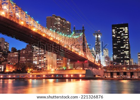 Queensboro Bridge over New York City East River at sunset with river reflections and midtown Manhattan skyline illuminated. 