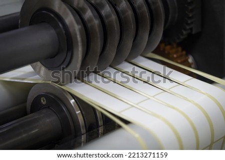 Rotating knives for cutting a self-adhesive label into several narrow ribbons. Equipment for the production of self-adhesive labels. Rotary die cutting machine with slitting blade. Selective focus Royalty-Free Stock Photo #2213271159