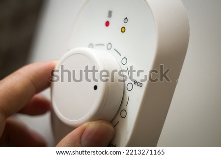 Setting the temperature controller of the heater in the eco mode of operation. Thermostat of a modern heater. A person turns the wheel of the temperature controller with his hand. Selective focus Royalty-Free Stock Photo #2213271165
