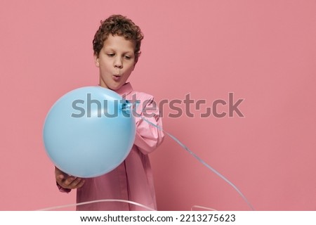 happy, funny boy in pink clothes on a pink background plays joyfully smiling with a blue balloon