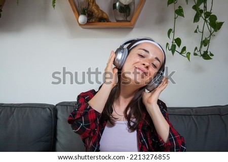 Young woman, sipping, sitting on the sofa, listening to music with headphones and dancing.