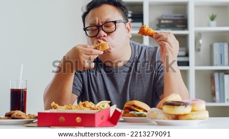 Asian fat man enjoy to eat unhealthy junk food, hamburger, pizza, fried chicken Royalty-Free Stock Photo #2213279091