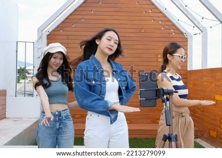 Young Asian woman with her friend er created her dancing video by smartphone camera together on rooftop outdoor at sunset To share video to social media application Royalty-Free Stock Photo #2213279099