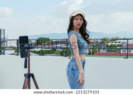 Young Asian woman created her dancing video by smartphone camera on rooftop outdoor at sunset. To share video on social media application Royalty-Free Stock Photo #2213279103