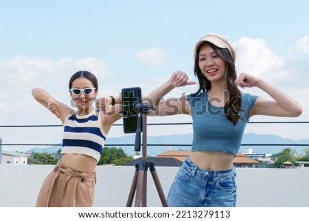 Young Asian woman with her friend er created her dancing video by smartphone camera together on rooftop outdoor at sunset To share video to social media application Royalty-Free Stock Photo #2213279113