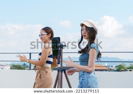 Young Asian woman with her friend er created her dancing video by smartphone camera together on rooftop outdoor at sunset To share video to social media application Royalty-Free Stock Photo #2213279115