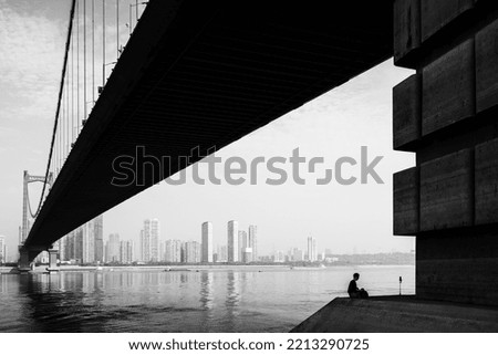 A man taking selfie photo under a huge bridge. The text on the bridge is the bridge name: Yingwuzhou Great Bridge.