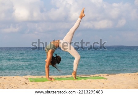 Full length shot of young woman practicing yoga on the beach outdoors.