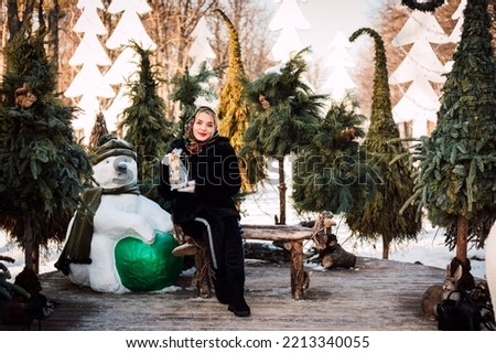 A woman in a national Ukrainian headscarf sits on a bench near Christmas trees