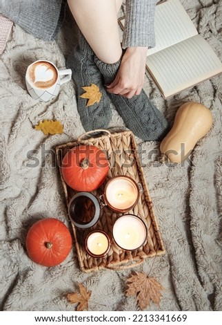 A girl in a sweater and knitted socks sits on a blanket. Cozy autumn concept. Pumpkins and candles on a tray near the girl.
