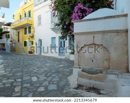 Greece Tinos island, Chora town. Cyclades building architecture, traditional street marble faucet, cobblestone street, bougainvillea plant.