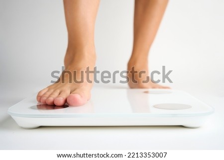 Woman legs stepping on floor scales, close-up. Female bare feet standing on scales, white background. Diet and overweight concept. 
