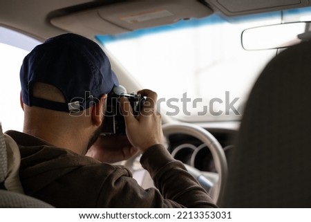 Private detective or paparazzi sitting inside the car, taking pictures with a reflex camera, inside view