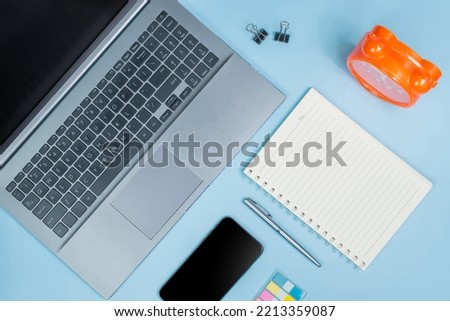 Top view of Office Table top with laptop computer, orange clock, notebook, smart phone on blue table. Business, Education, Office concept and design
