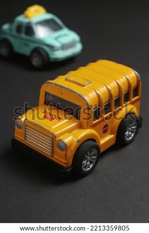 close up photo of a yellow school bus toy on asphalt with blurred taxi toy background. school bus miniature for kids play