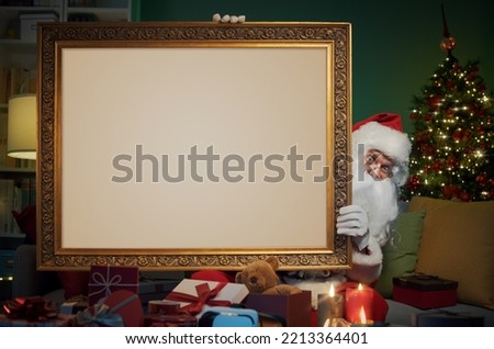 Santa Claus at home holding a big blank painting with elegant golden frame