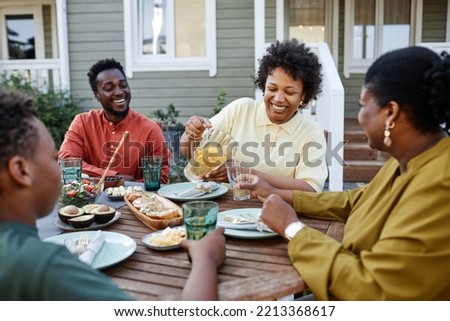 Portrait of smiling black woman pouring lemonade drinks to glass during family gathering outdoors