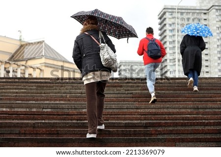 Women with umbrellas walking up the steps on city buildings background. Rain in autumn city