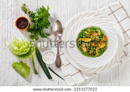 petits pois, french dish of tender, new-season peas braised in chicken stock with lettuce, onion bulbs and speck, cut into lardons, served in white bowl, flat lay