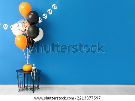 Table with skeleton, Halloween pumpkin and balloons near blue wall