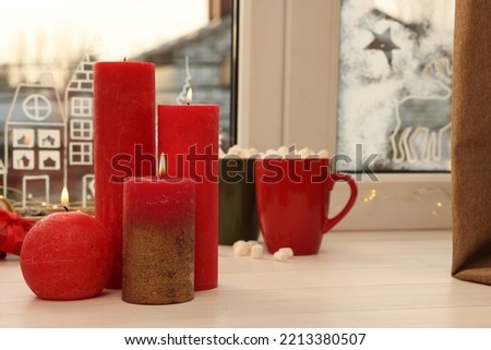 Beautiful burning candles with Christmas decor on white wooden table near window, space for text
