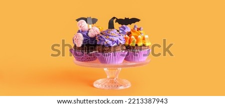 Stand with tasty Halloween cupcakes on orange background