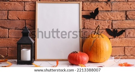 Blank photo frame with Halloween pumpkins, lantern and autumn leaves on table near brick wall